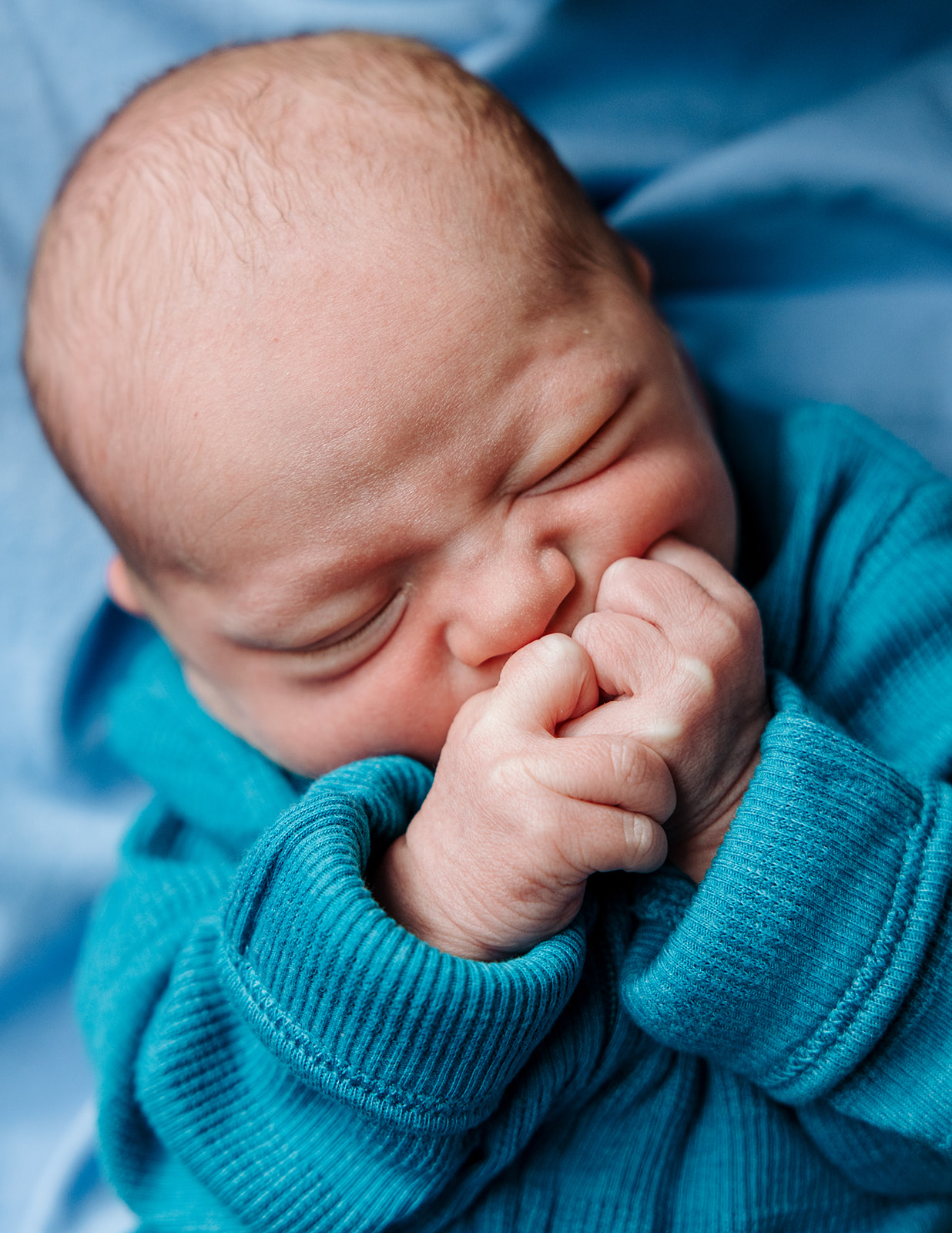 tight photo of newborn baby boy squishing his fists to his mouth