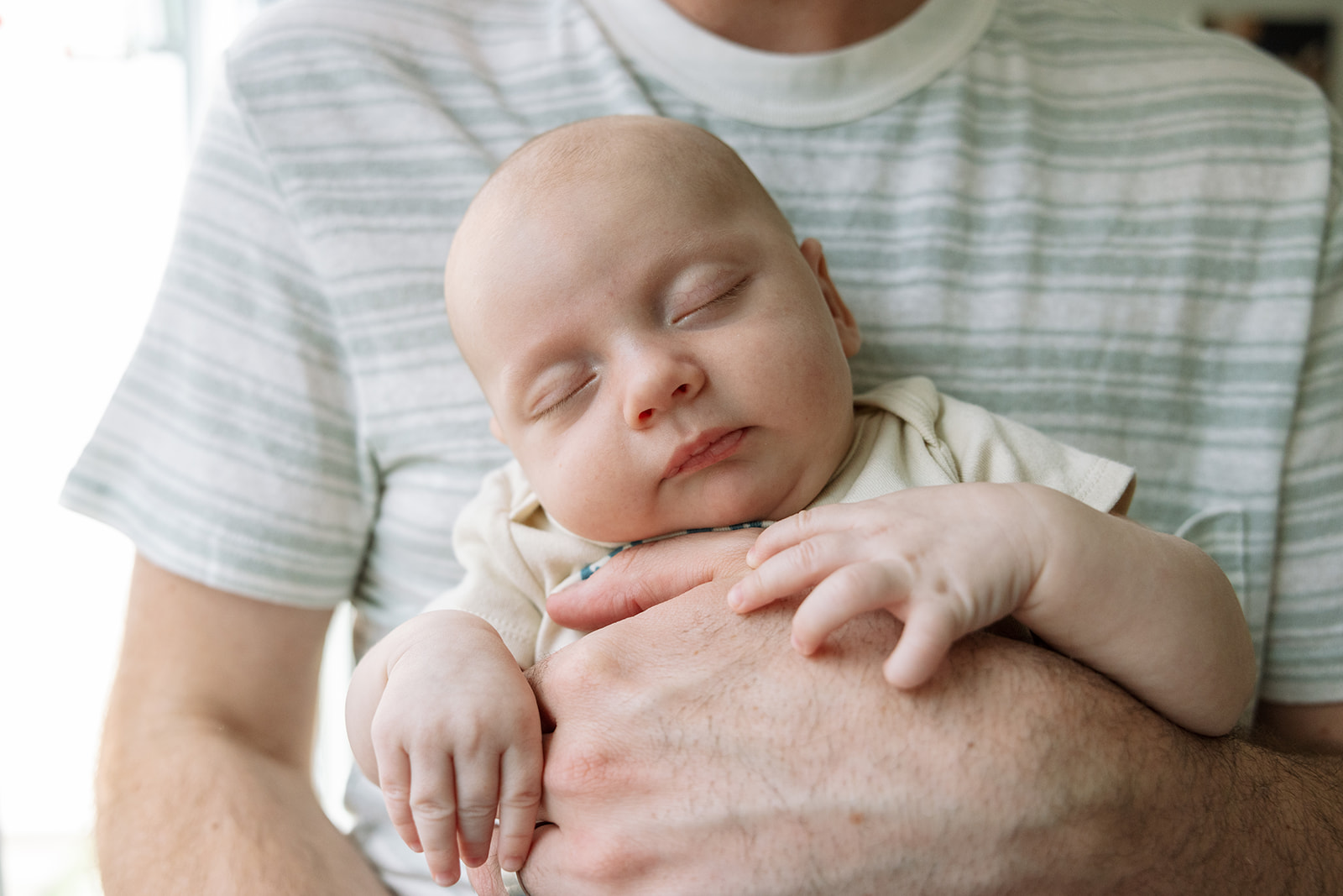 photo of newborn baby sleeping and facing the camera while dad holds him against his chest