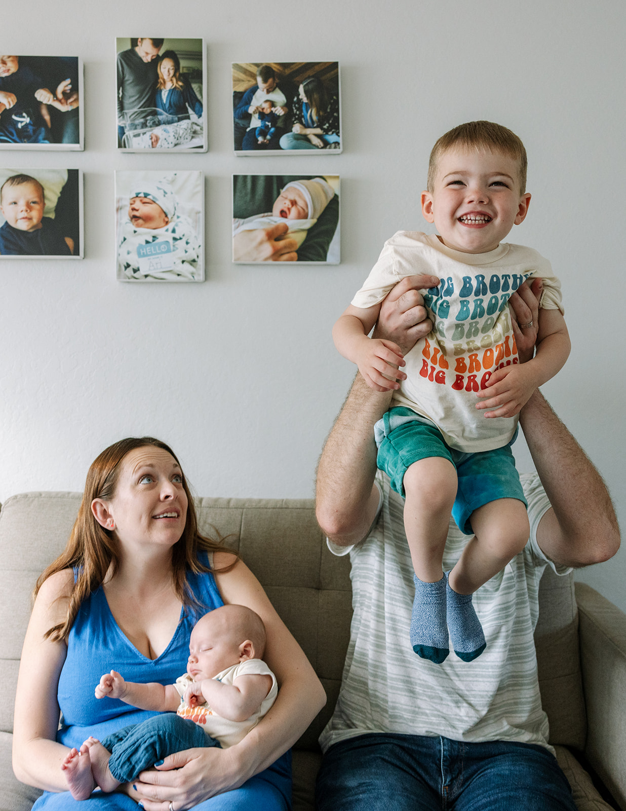 dad lifting toddler up in the air while sitting on the couch with mom holding newborn and looking up at toddler