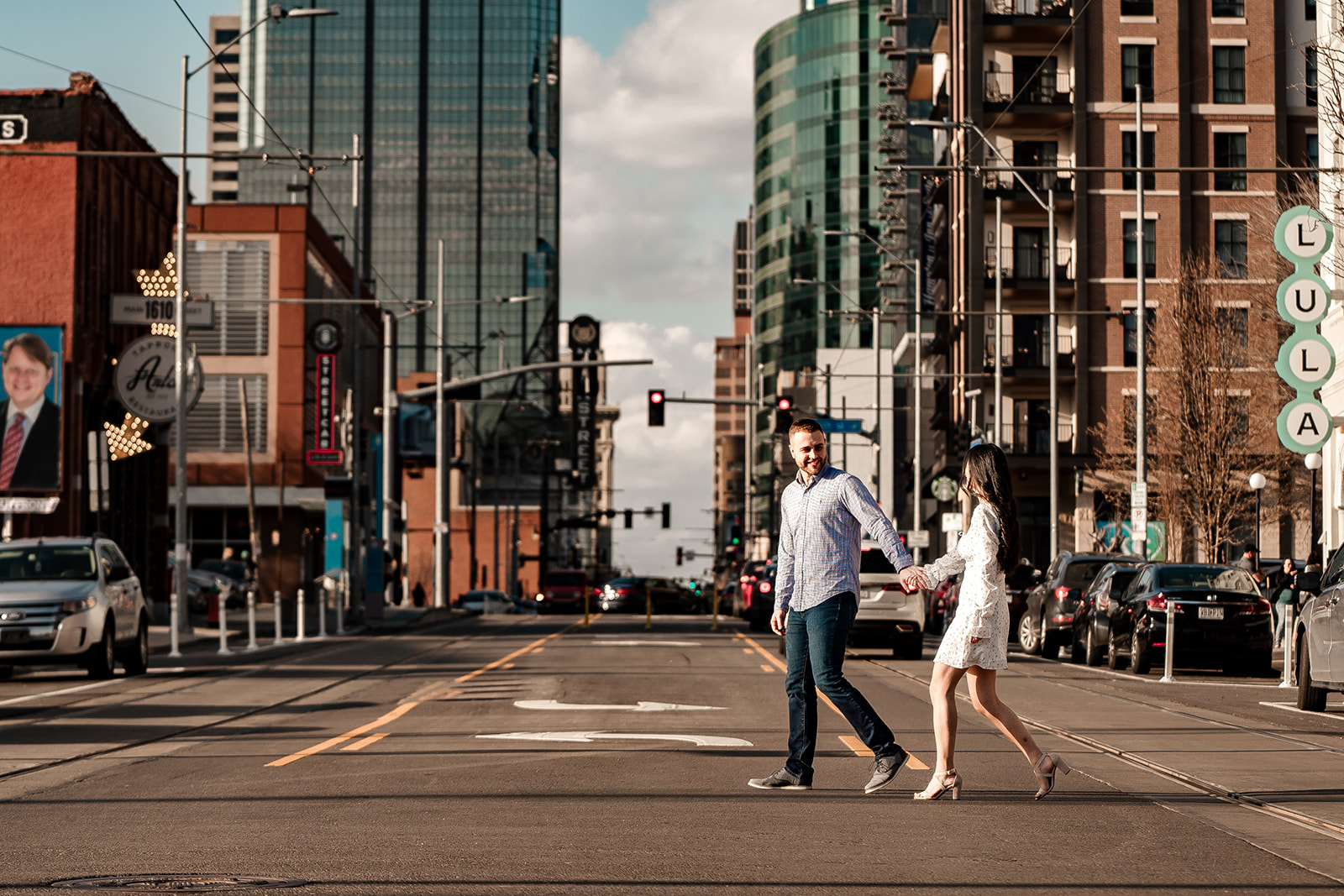 couple walking across road in Crossroads Kansas City for engagement photo shoot