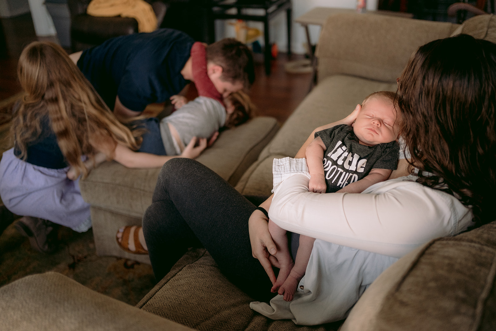 mother holds newborn while father plays with kids in the background