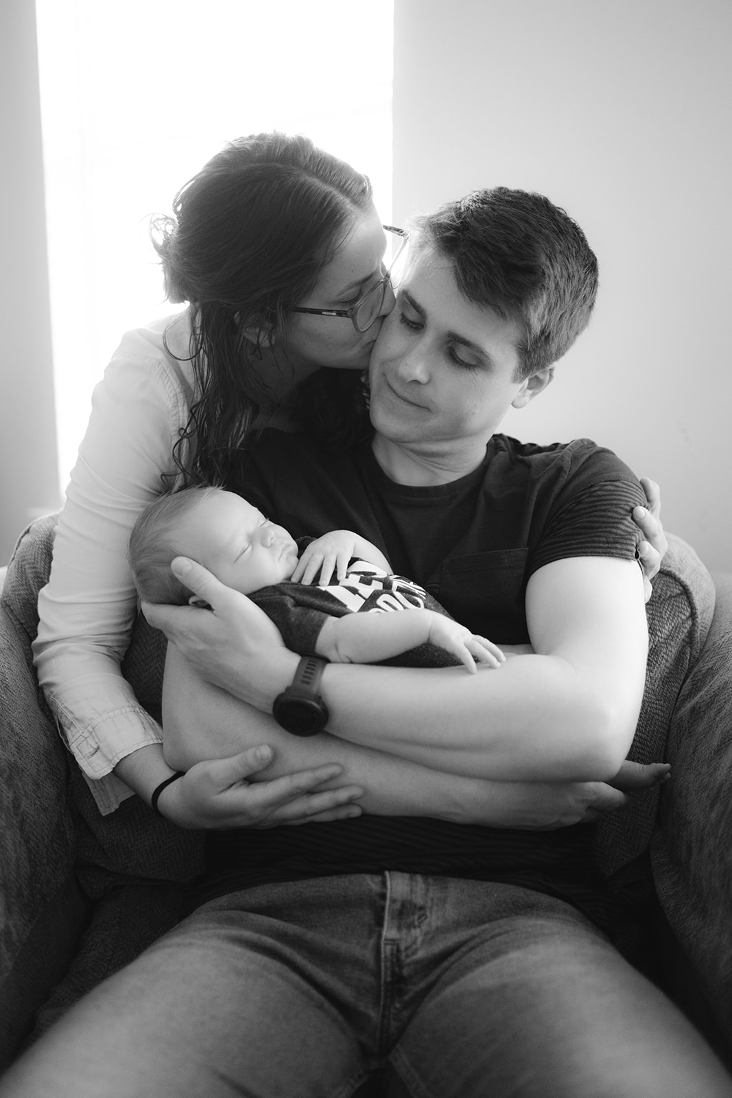 wife kisses husband while holding their newborn baby