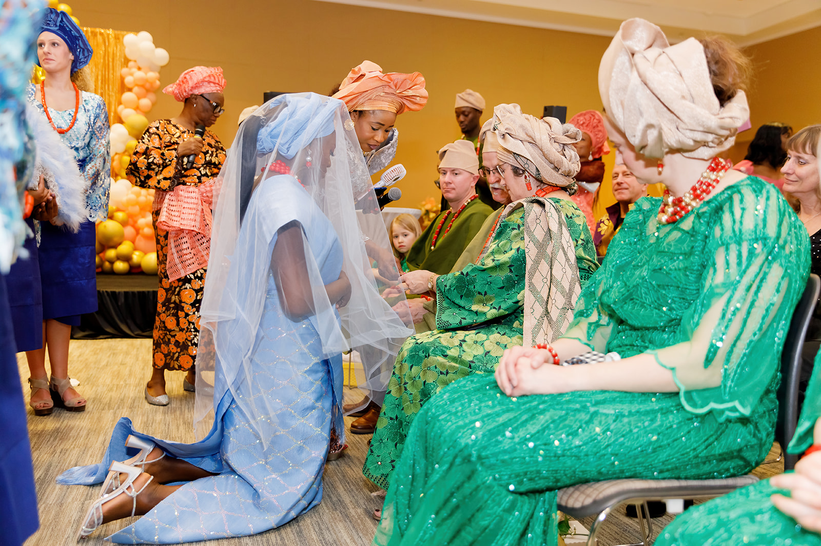 Bride kneels down in front of her family-in-law Nigerian traditional wedding at Truhlsen Campus Events Center at UNMC