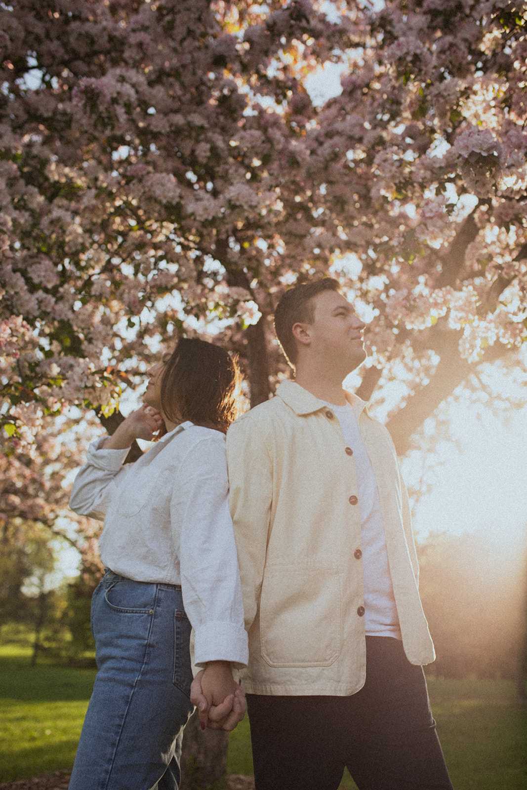 a couple standing together at sunrise beneath flower trees with the sunrise behind them