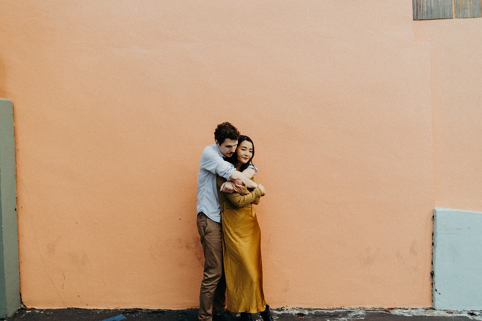 couple snuggling in front of coral colored building