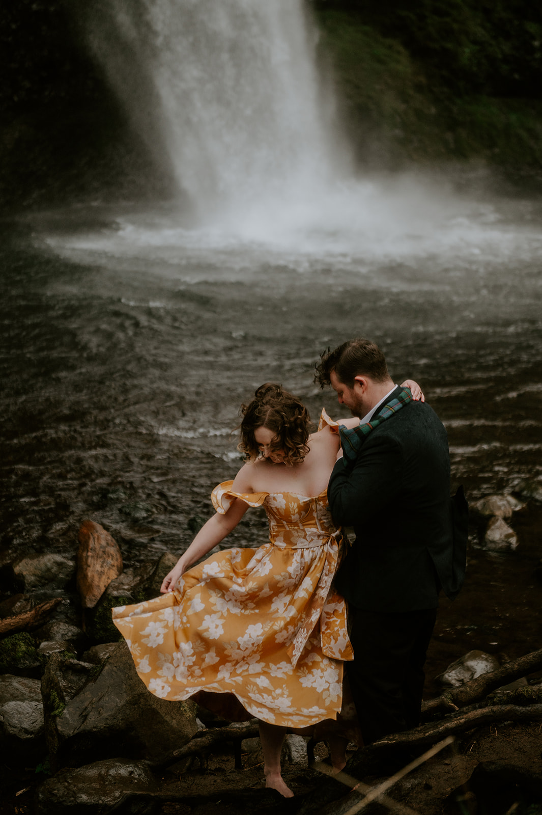A couple standing at the base of a waterfall in formal clothes outside of portland