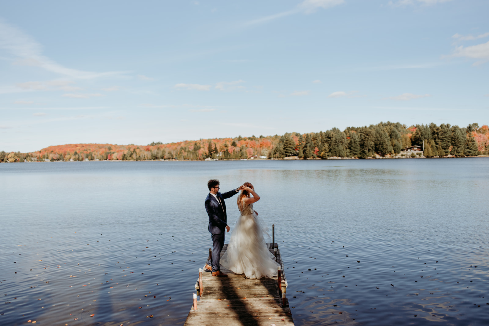 A bride and groom on their honeymoon dancing at the end of a dock with fall colours across the lake.