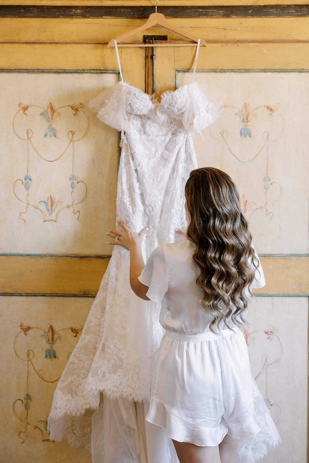 bride looks at her dress handing on the wall