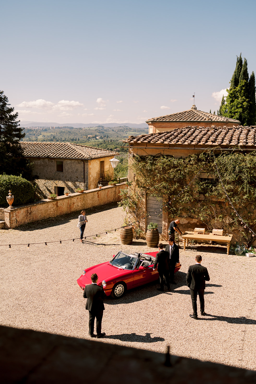 men surround a red sports car in an Villa Catignano courtyard