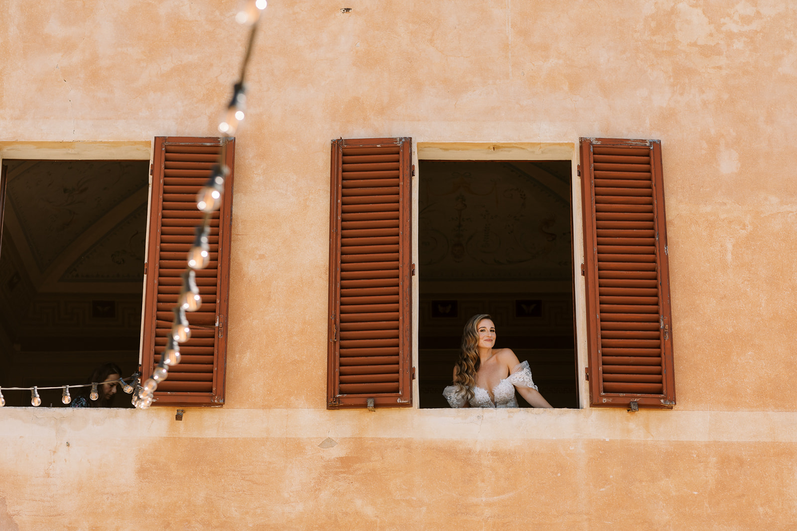 bride looks out shuttered windows at italy wedding at Villa Catignano