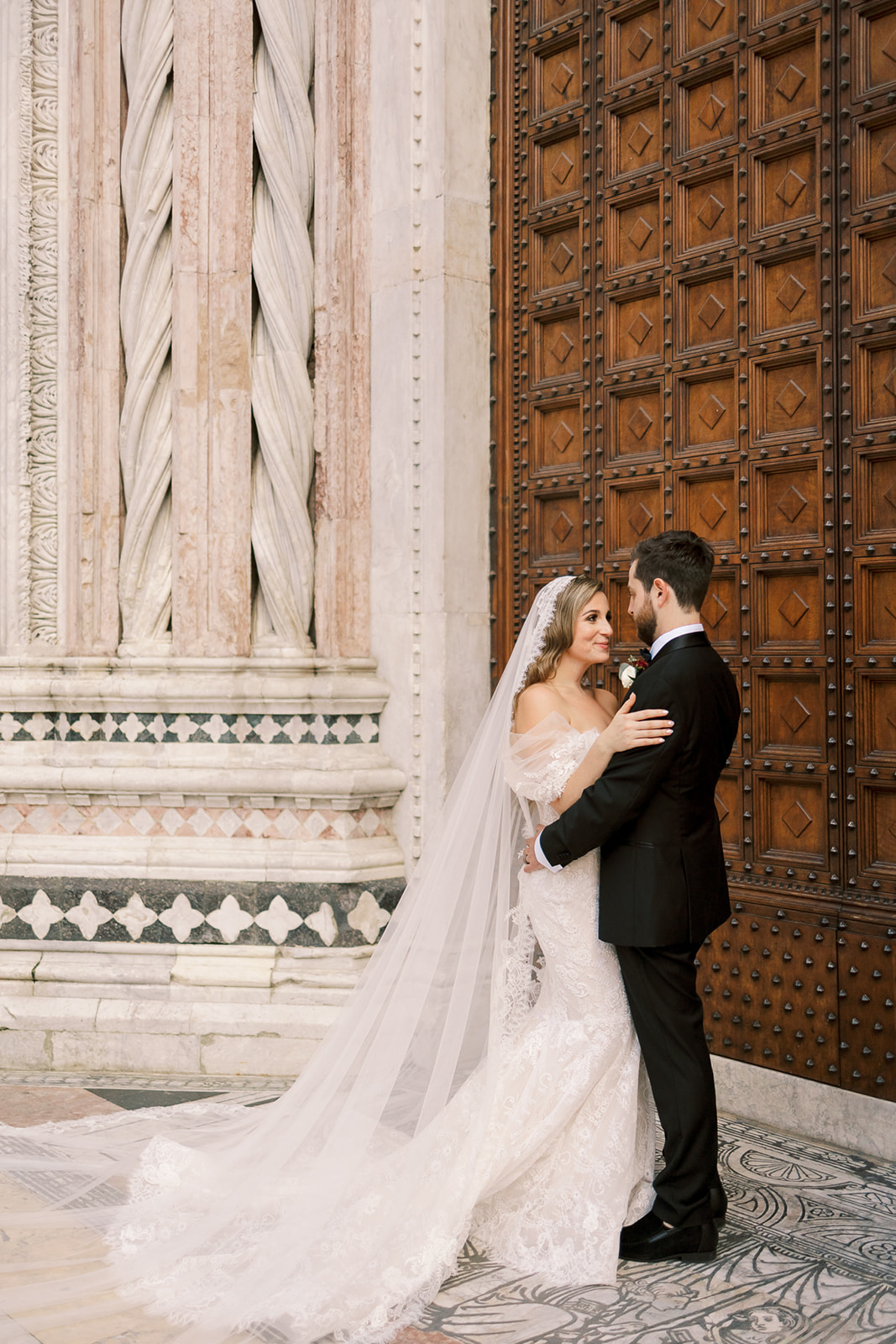 bride and groom pose together in front of grand Italian doors 