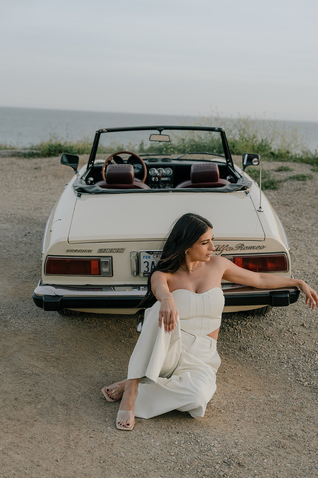 a woman sits in front of a vintage car in the hills of Malibu