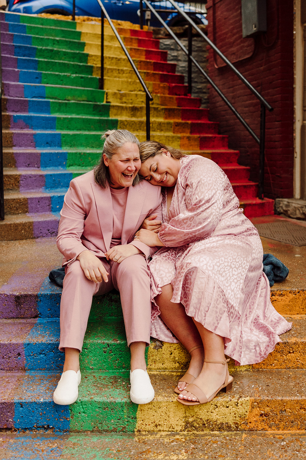 Women holding each other while sitting on rainbow stairs during their city engagment session