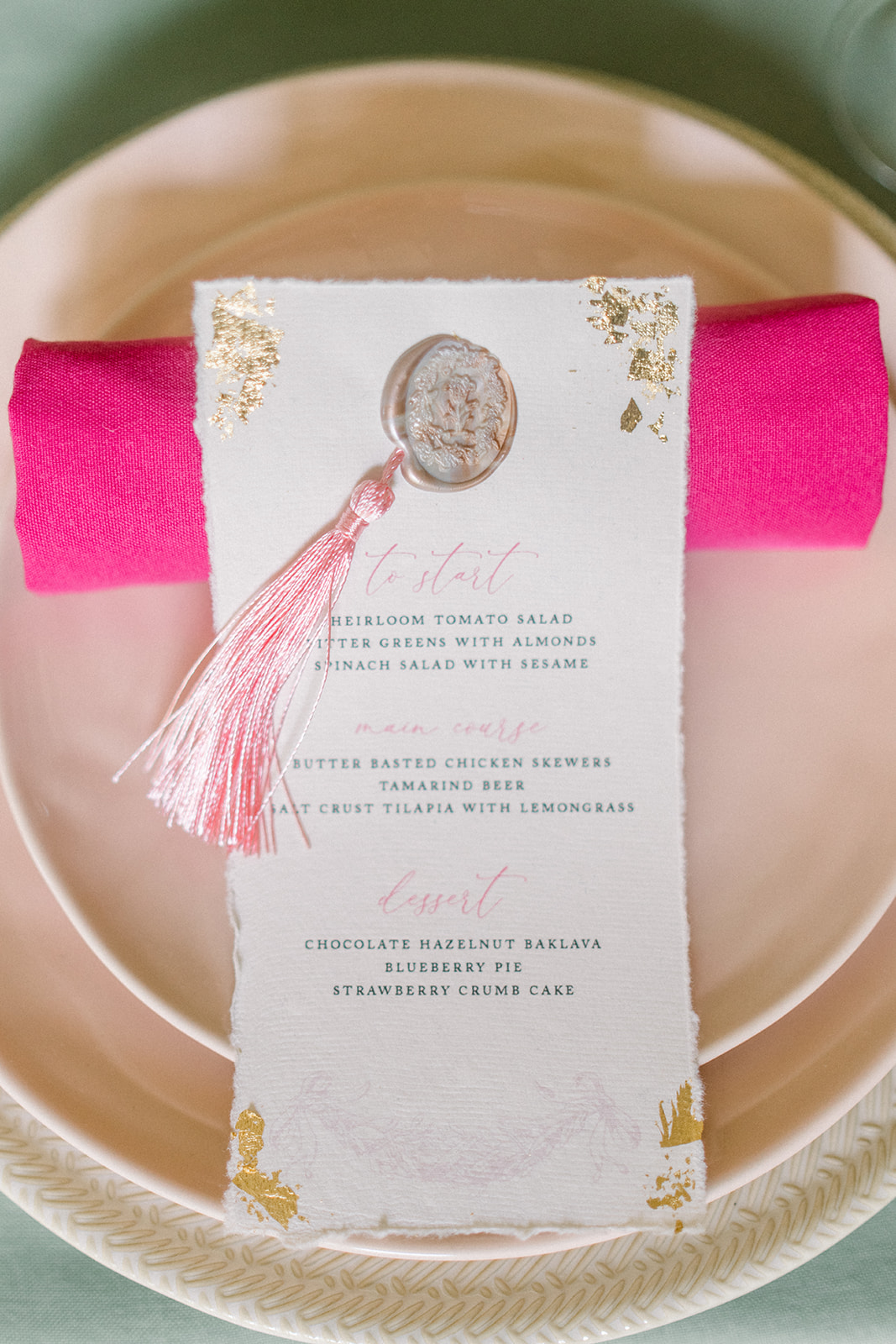 Luxury wedding table setting featuring a pastel pink charger plate, gold cutlery, and an elegant invitation