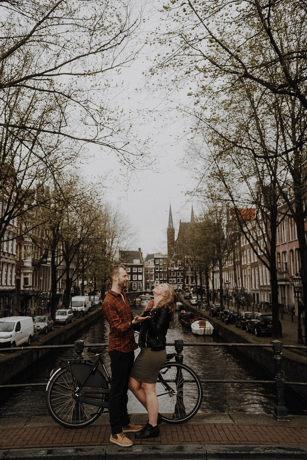 Couple laugh on Amsterdam canal bridge during maternity session