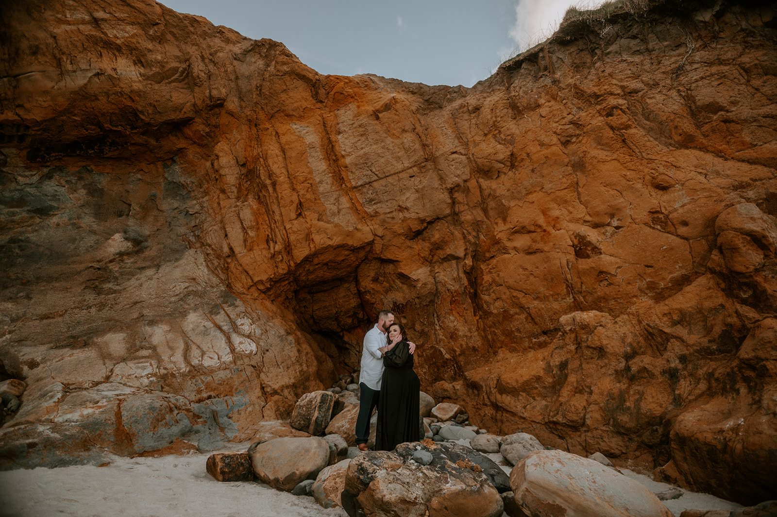 Couple kissing in front of orange rocks at Cape Kiwanda