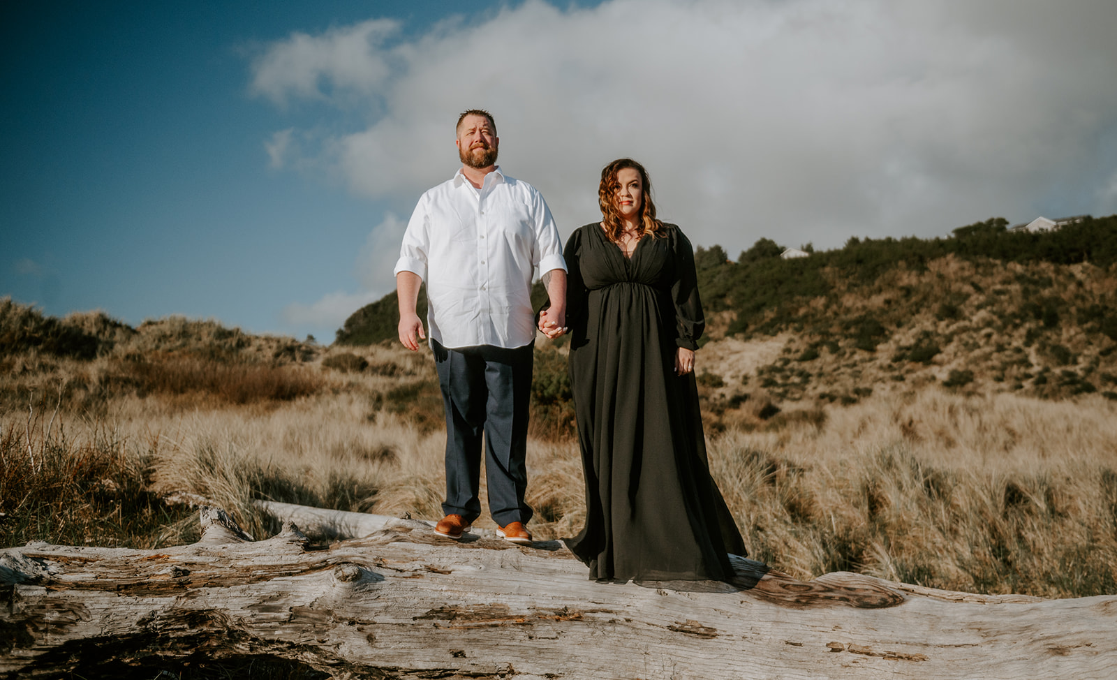 Couple standing on a piece of driftwood dressed nice for their engagement photos