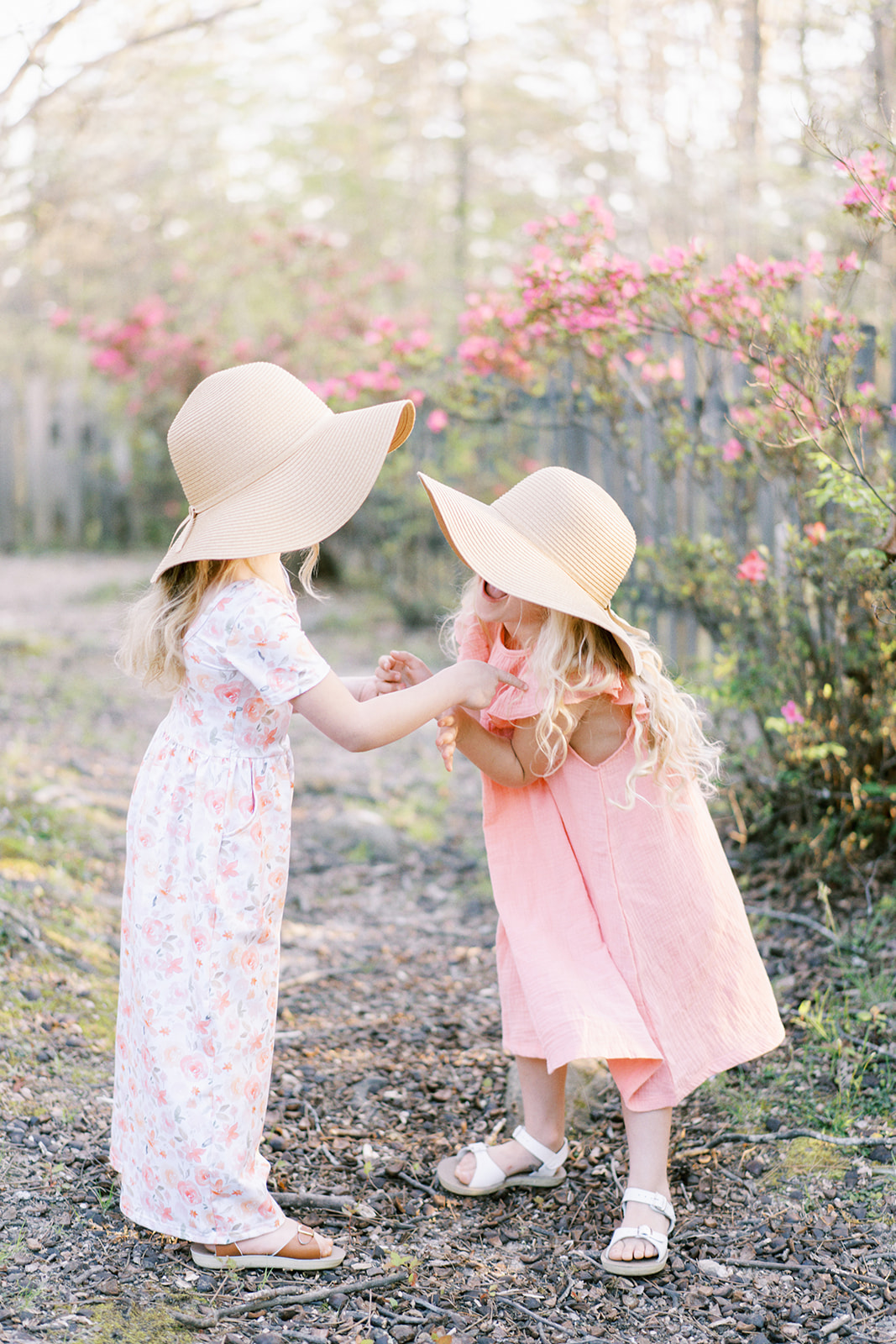 Two young girls with hats on laugh in front of the spring flowers at Sallie Howard Memorial Church in Mentone Alabama