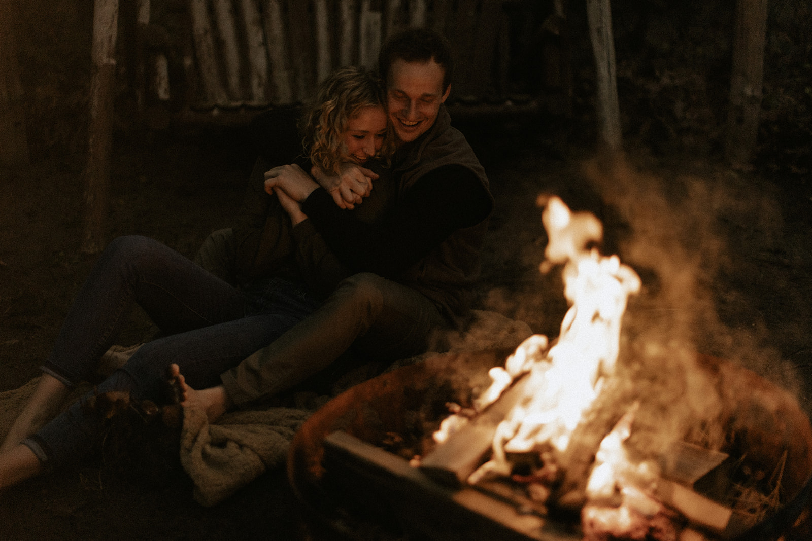 A couple sitting next to a campfire and cuddling 