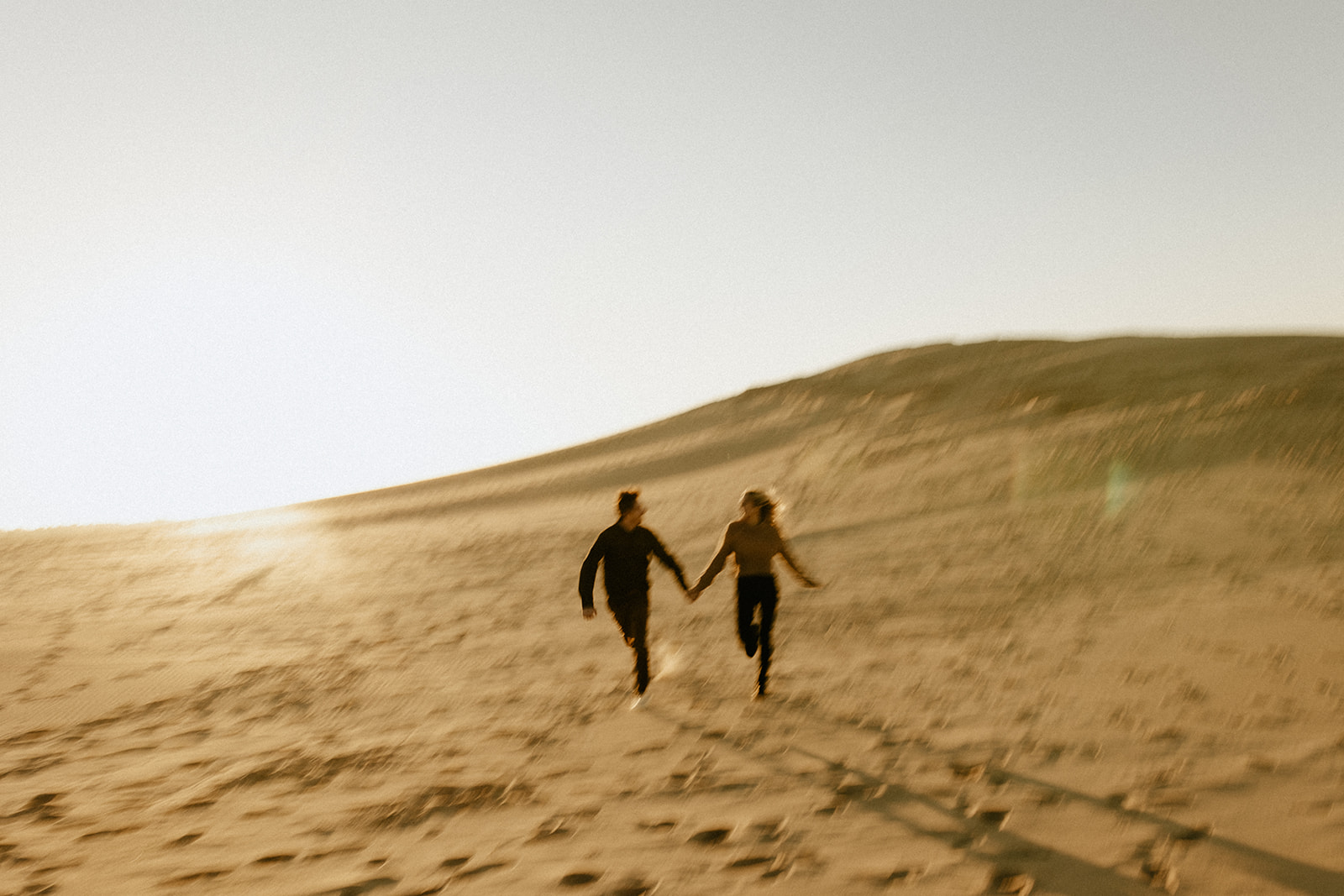 A couple holding hands and running at Silver Lake Sand Dunes in Mears, Michigan