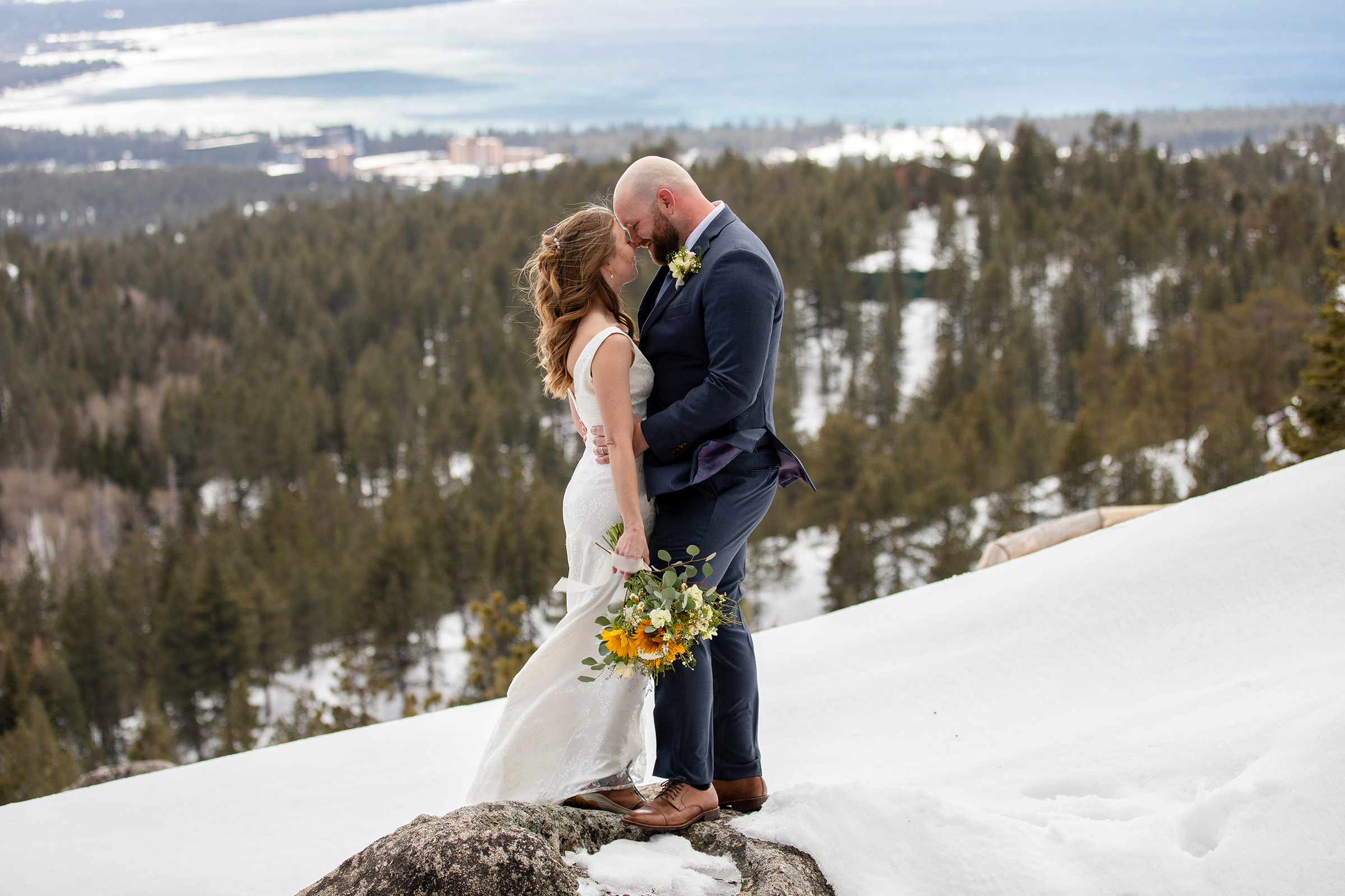 Bride and groom facing each other, kissing with Lake Tahoe in the background.