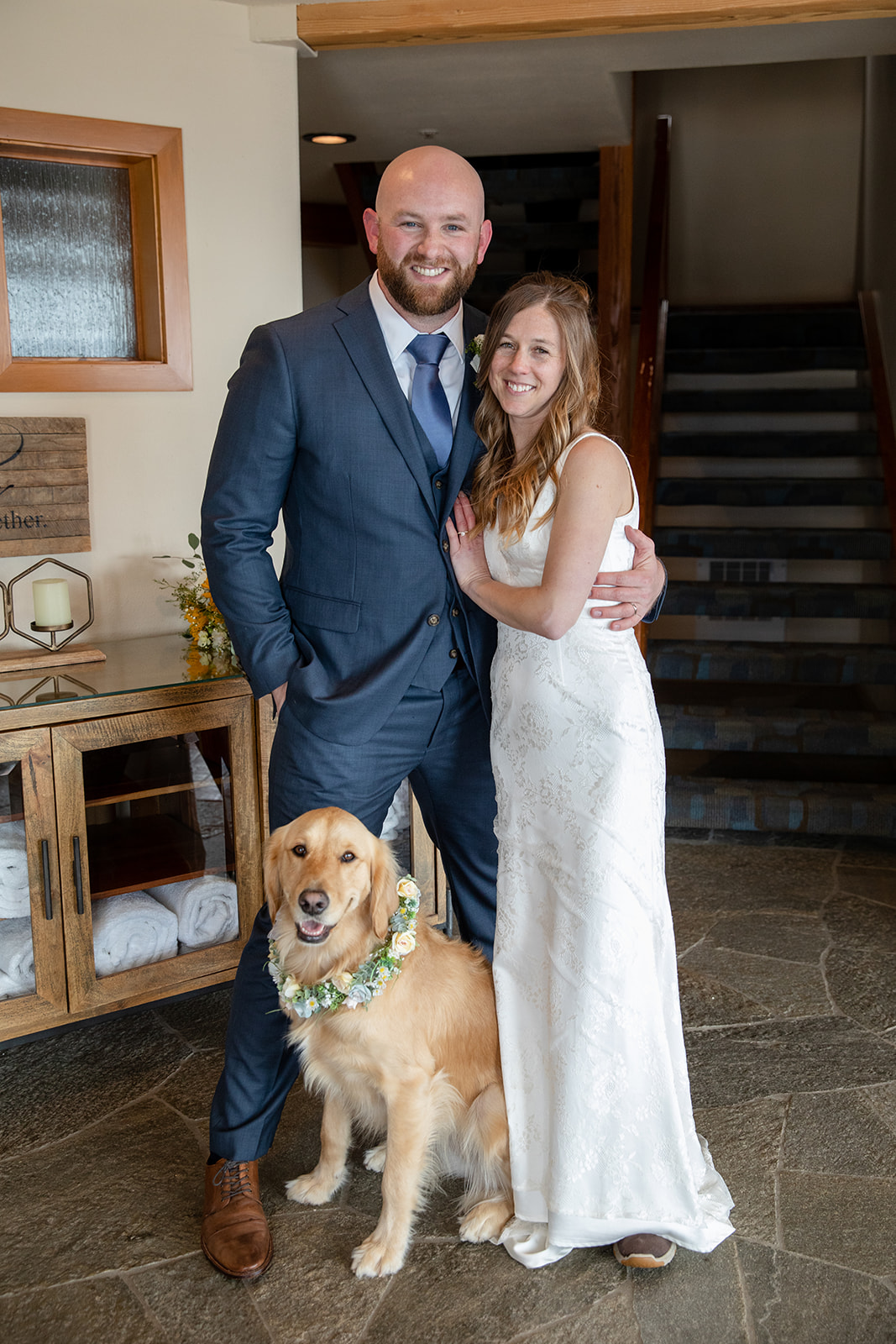 Wedding couple posing for a portrait with their Golden Retriever wearing a flower collar. 